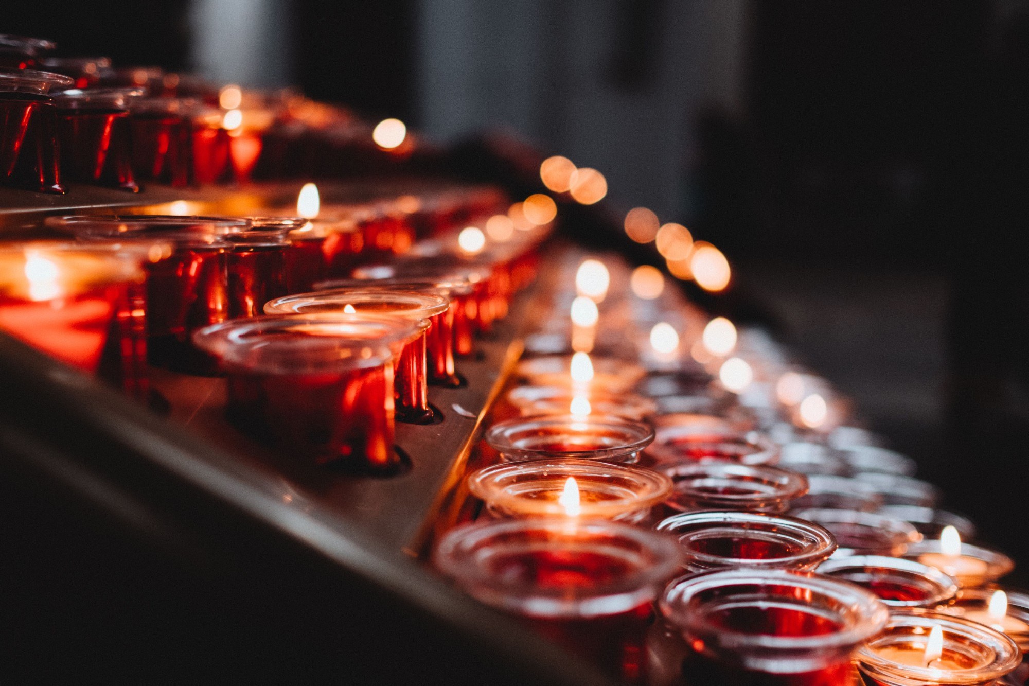 Des rangées de bougies rouges allumées dans une église.